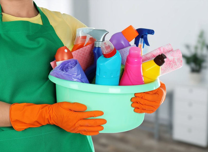Woman holding basin with cleaning supplies in office, closeup