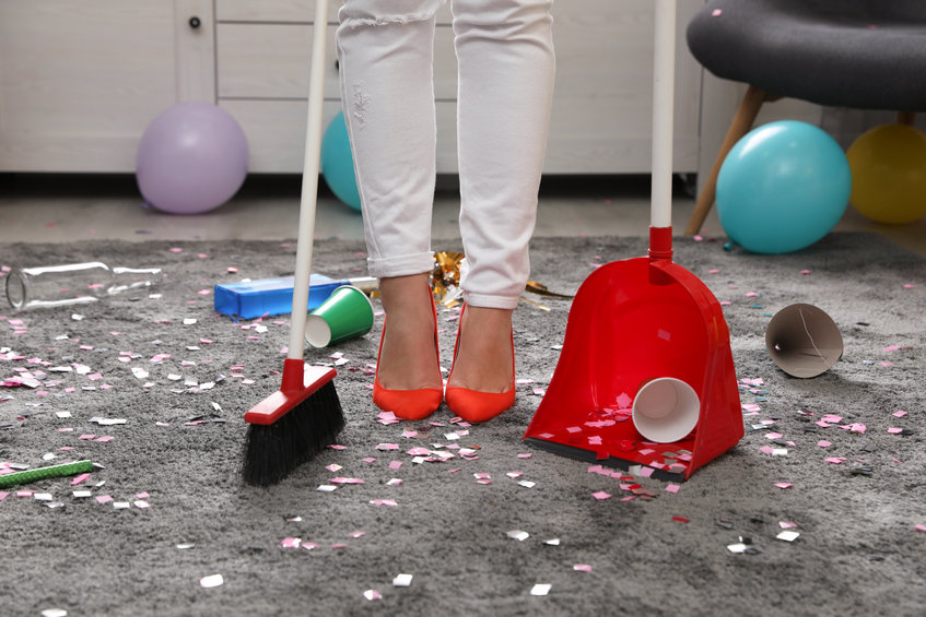 Woman with sweep broom and dust pan cleaning messy room after party