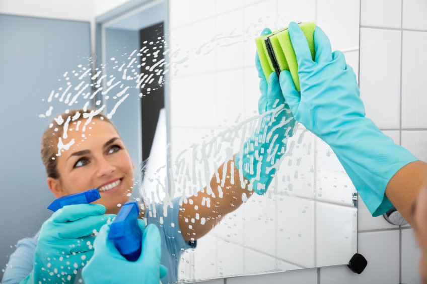 Smiling Woman Cleaning The Mirror Of The Bathroom